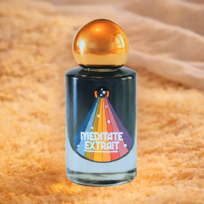 A bottle of Meditate Extrait fragrance with a dark glass body, a metallic gold spherical cap, and a colorful rainbow party hat graphic on the front.