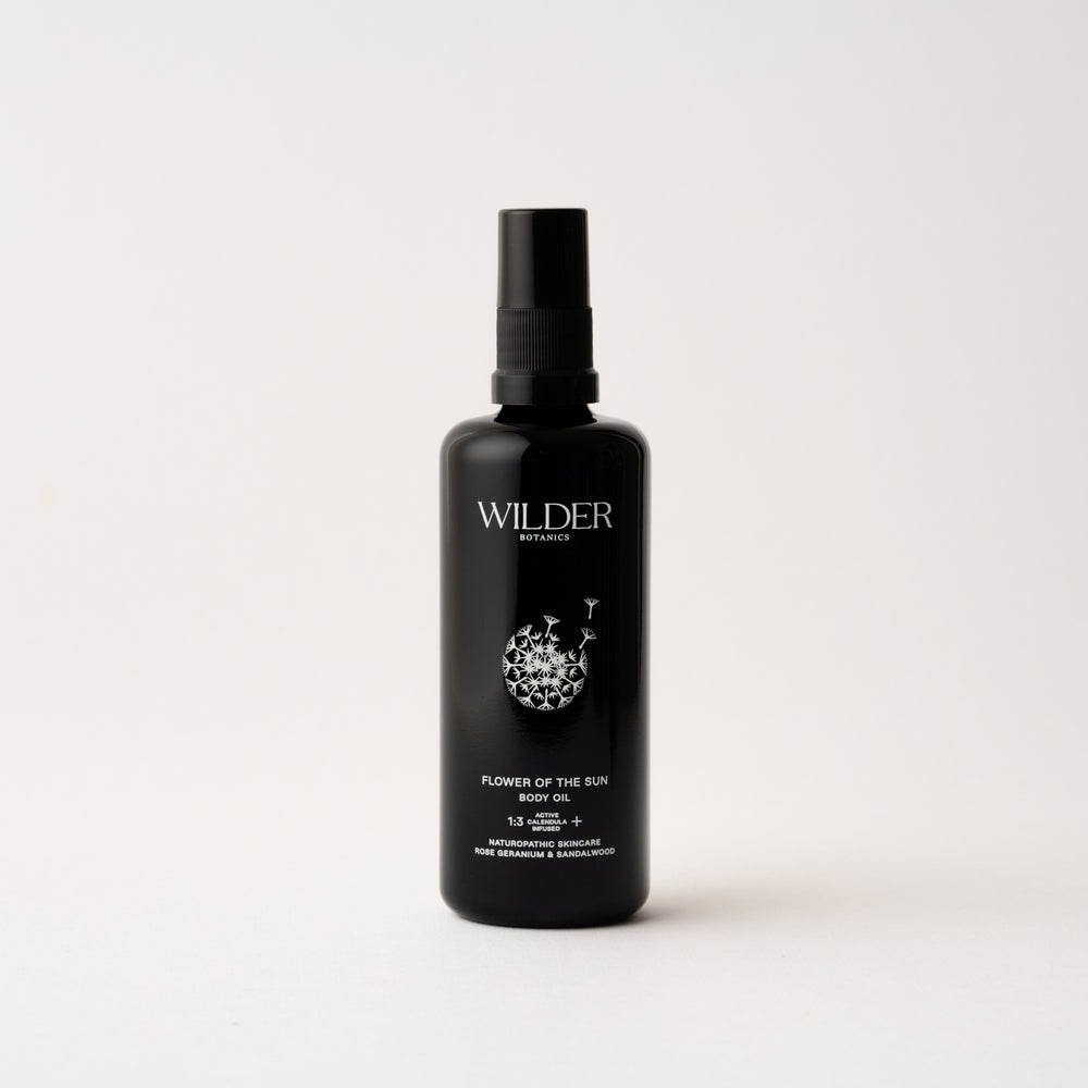 Wilder Botanics Flower of the Sun Body Oil bottle surrounded by natural elements, highlighting its woody and floral ingredients. The oil is presented in eco-friendly packaging, conveying hydration, nourishment, and wellness for all skin types.