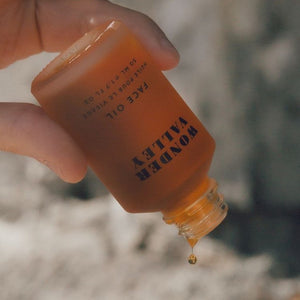Hand holding a bottle of 'Valley Wonder' face oil with a blurred natural background