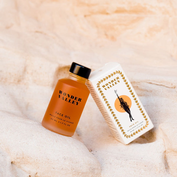 Orange face oil bottle by Wonder Valley and white box with gold design on a beige textured background