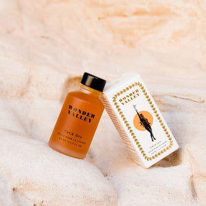 Orange face oil bottle and white box with gold design on a beige textured background