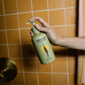 Hand holding a green bottle labeled 'Wonder Valley' against an orange tiled wall.