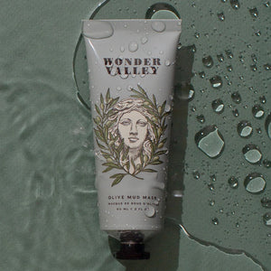 Tube of Wonder Valley Olive Mud Mask on a wet surface with water droplets.