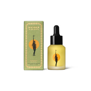 Clear glass bottle and green box of Wonder Valley hair oil on a white background