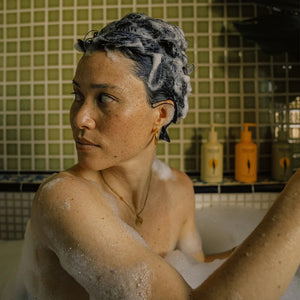 Person taking a bubble bath with shampooed hair in a tiled bathroom.