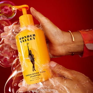Yellow shampoo bottle labeled 'Wonder Valley' held by a hand against a red background with bubbles.