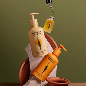 Two bottles of Wonder Valley shampoo and conditioner with a hair oil on a green background