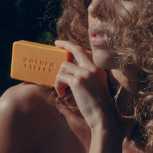 A woman holding a yellow bar of soap with 'Wonder Valley' branding.