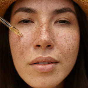 Close-up of a woman's face with a dropper applying liquid to her skin.