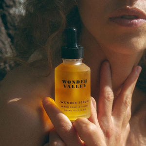 A woman holding a bottle of 'Wonder Valley' wonder serum close to her face.
