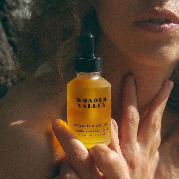 A woman holding a bottle of 'Wonder Valley' wonder serum close to her face.
