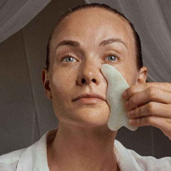 Woman using a gua sha tool on her face with a neutral background. YIN YOUR SKIN LAHJA Gua Sha Facial Tool